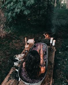 a woman sitting in a bathtub next to a campfire with candles on it