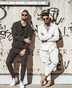 two men in white suits and sunglasses leaning against a wall with graffiti on the walls