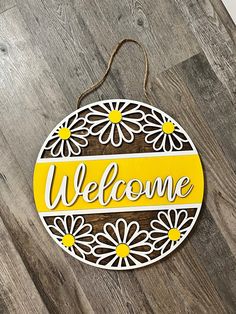 a wooden sign that says welcome with daisies on the front and bottom, hanging on a wood floor