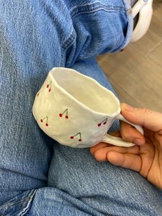 someone is holding a coffee cup with cherries painted on the bottom and sides in their hands