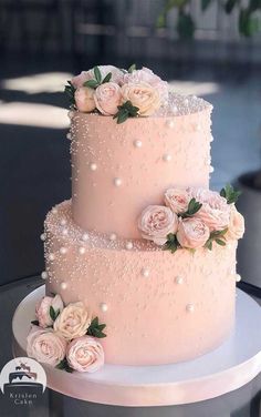 a three tiered pink wedding cake with flowers on the side and pearls around the edges