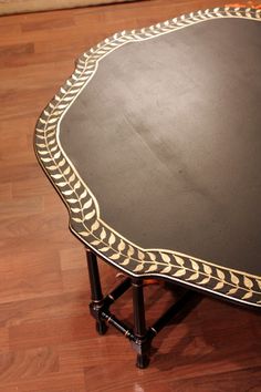 a black table with gold trim on it sitting on a hard wood floor next to a wall