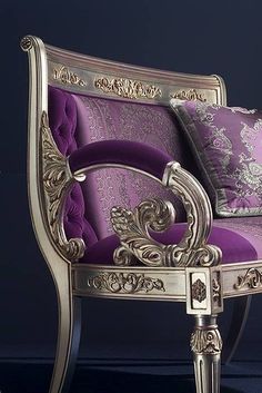 an ornate chair with purple and gold pillows on it's arm rests against a black wall