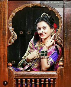 a woman in a purple and gold sari posing for the camera with her hands on her chest