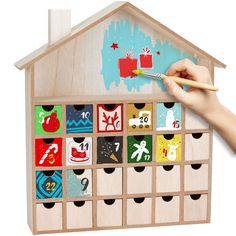 a child's hand is holding a pencil and drawing on a wooden toy house