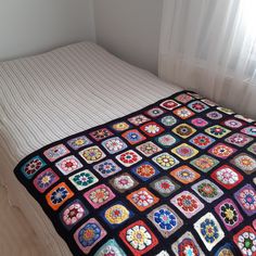 a bed covered in a multicolored blanket next to a white wall and window