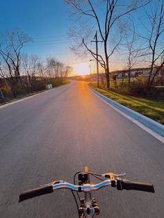 the sun is setting on an empty street as seen from a bicycle's handlebar