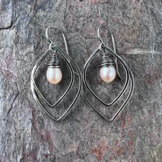 A pair of genuine freshwater pearls are carefully wrapped in sterling silver wire. The luminous pearls are very pale peach in color. The pair is framed by sterling silver petal shapes which I have formed, soldered, and textured by hand. The earrings hang from handformed Sterling Silver earwires. The silver has been oxidized and polished to create the patina finish. Be sure to see all photos and video for size and color reference. Total Earring Length: About 1 and 3/4" Handmade Silver Pearl Earrings In Pear Shape, Handmade Silver Pear-shaped Pearl Earrings, Delicate Teardrop Wire Wrapped Pearl Earrings, Silver Teardrop Wire Wrapped Pearl Earrings, Pale Peach, Color Reference, Patina Finish, Handmade Sterling Silver, Silver Wire