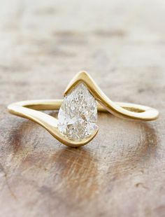 a yellow gold ring with a pear shaped diamond in the center on a wooden surface