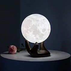 the moon lamp is sitting on top of a small table next to a rose flower