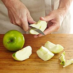 a man cutting up an apple on top of a wooden table next to sliced apples