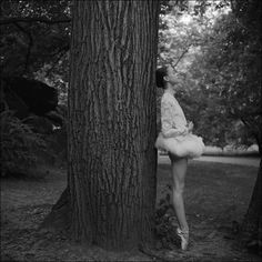 a ballerina leaning against a tree in black and white