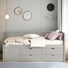 a white bed sitting under a window next to a wall mounted clock and two round mirrors