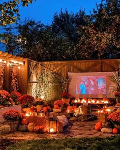 an outdoor movie screen surrounded by pumpkins, candles and flowers in the garden at night