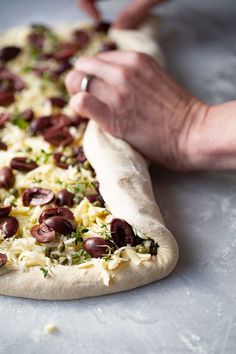 someone is making a pizza with olives and cheese