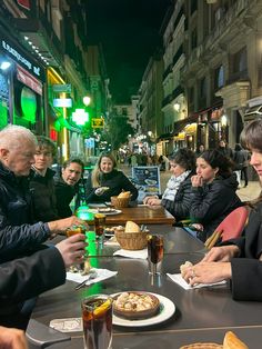 several people sitting at a table eating pizza and drinking sodas on the street side