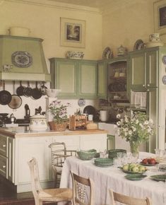 an old fashioned kitchen with green cabinets and white table cloths on the dining room table