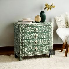 a green and white painted chest of drawers with flowers on the top, next to a chair