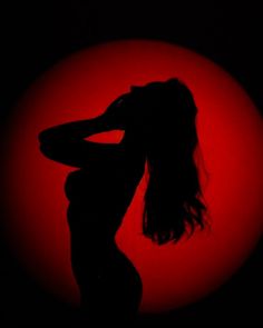 the silhouette of a woman in front of a bright red sun with her hair blowing back