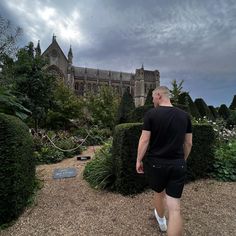 a man walking in front of a building with lots of trees and bushes around it