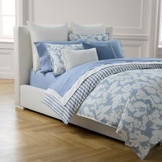 a bed with blue and white comforters in a room next to a window on a hard wood floor