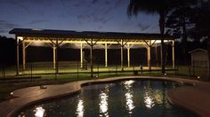 a gazebo lit up at night next to a swimming pool with lights on it