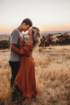 a man and woman kissing in the middle of an open field with tall dry grass