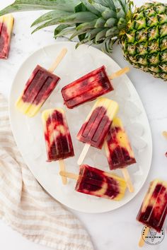 pineapple and raspberry popsicles on a plate next to a pineapple