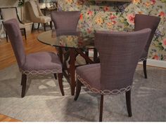 a dining room table with purple chairs and a floral wallpaper behind the glass top