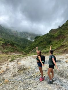 two people standing on the side of a mountain with their arms up in the air