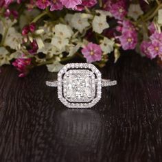 a diamond ring sitting on top of a wooden table next to purple and white flowers