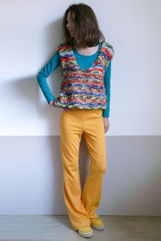 a woman standing in front of a white wall wearing yellow pants and a blue top