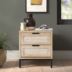 a wooden cabinet with two drawers next to a potted plant and framed pictures on the wall