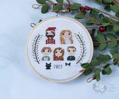 a cross stitch ornament with four different people on it and holly branches in the background