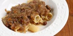 a white plate topped with pasta covered in meat and sauce on top of a wooden table