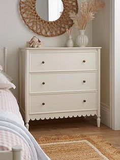 a white dresser sitting next to a bed under a mirror on top of a wall