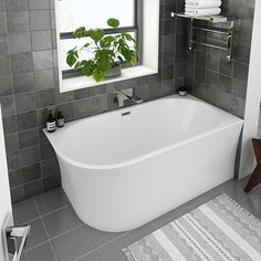 a white bath tub sitting next to a window in a bathroom with gray tiles on the walls