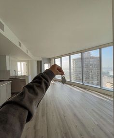 a person's hand reaching out towards an empty room with large windows and wood flooring