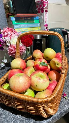 a wicker basket filled with apples on top of a table next to flowers and books