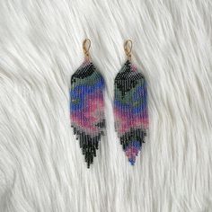 pair of beaded earrings on white fur with black and pink feathers in the background