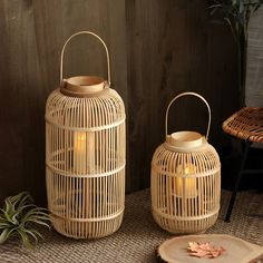 two wicker lanterns sitting on top of a table next to a wooden plate and potted plant