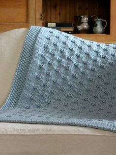 a blue crocheted blanket sitting on top of a couch next to a book shelf