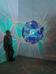 a man standing in front of a blue and green light fixture hanging from the ceiling