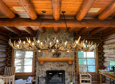 a rustic log cabin living room with deer antlers hanging from the ceiling and fireplace