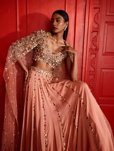 Dusty peach flowy lehenga hand embellished with our coin & pearl embellishment in a linear format, with a heavily embellished waist band. Paired with a coin & pearl embellished sleeveless crop & a heavily embellished matching net cape with power shoulders.From Shloka Khialani's Afterglow CollectionDELIVERY TIMEPlease allow 8-12 weeks for your outfit to arrive.FABRIC DETAILSGeorgette, Net, CrepeSpot Dry Clean Only. Glamorous Chinon Lehenga For Wedding, Glamorous Sequined Lehenga In Chinon, Designer Peach Lehenga With Mirror Work, Embellished Peach Lehenga For Reception, Glamorous Chinon Lehenga For Festive Season, Embellished Wedding Sets, Peach Sets With Mirror Work For Reception, Peach Reception Sets With Mirror Work, Peach Reception Set With Mirror Work