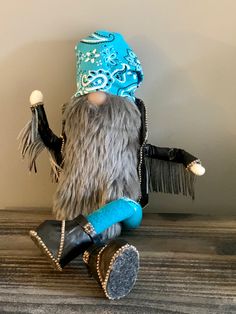 an old fashion doll sitting on top of a wooden table wearing a blue hat and black boots