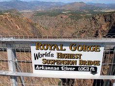 a sign that is on the side of a metal fence with mountains in the background