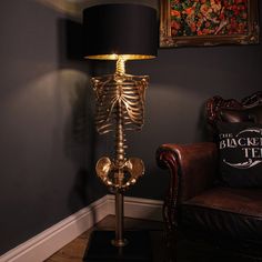 a gold skeleton lamp sitting on top of a wooden table next to a brown chair