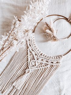 a white dream catcher with feathers and flowers in it on a tablecloth next to dried plants