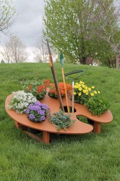 a wooden table with flowers and gardening tools on it in the middle of some grass